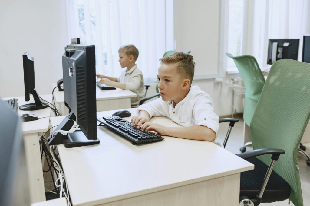Two young boys focused on computers in a bright, modern classroom setting.
